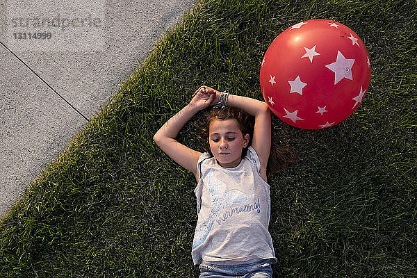 Draufsicht auf ein im Gras liegendes Mädchen mit Ballon im Hinterhof
