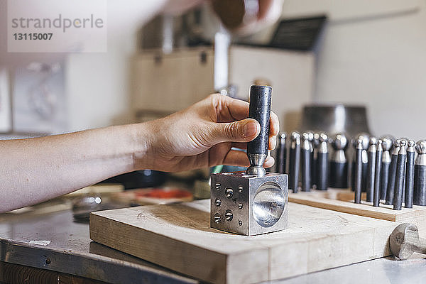 Beschnittene Hände eines Handwerkers mit Handwerkzeugen bei der Herstellung von Schmuck auf dem Tisch in der Werkstatt