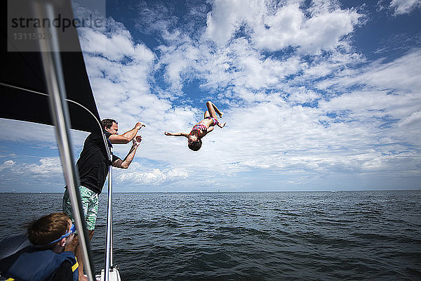 Vater und Sohn sehen ein Mädchen  das bei bewölktem Himmel ins Meer springt