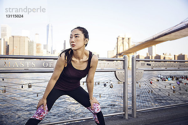 Nachdenkliche Sportlerin trainiert auf der Promenade mit der Brooklyn Bridge und dem One World Trade Center im Hintergrund