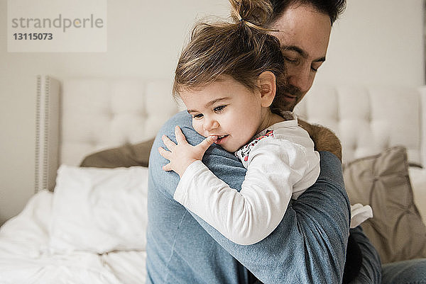 Liebender Vater umarmt Tochter zu Hause im Bett