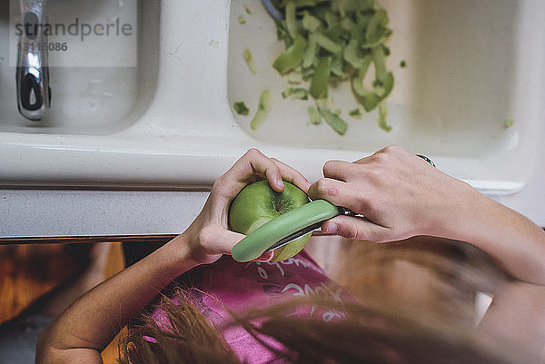 Hochwinkelaufnahme eines Mädchens  das zu Hause einen grünen Apfel schält