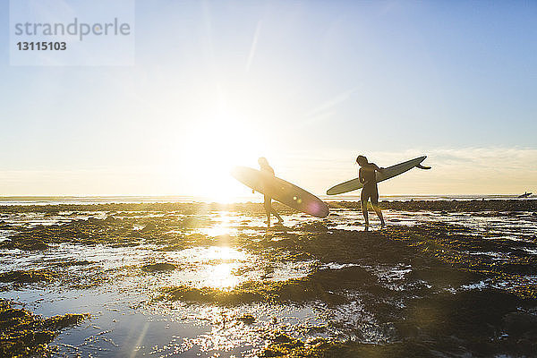 Ehepaar mit Surfbrettern beim Spaziergang am Strand des Bundesstaates San Onofre im Urlaub