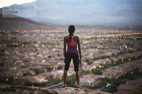 Rückansicht einer Frau  die auf einem Hügel steht und auf eine beleuchtete Landschaft schaut