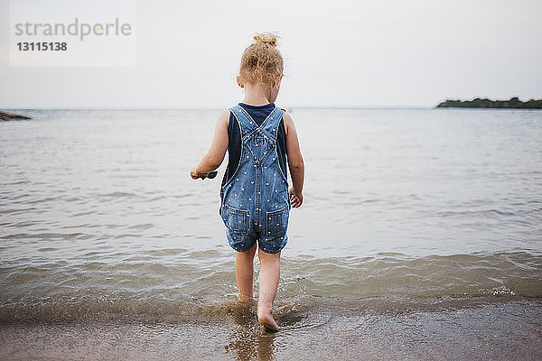 Rückansicht eines Mädchens  das am Strand im Meer vor klarem Himmel spazieren geht
