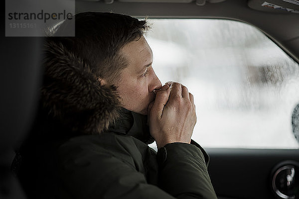 Seitenansicht eines im Auto sitzenden Mannes mit Händen auf dem Mund