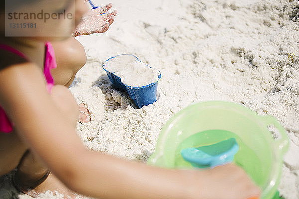 Hochwinkelaufnahme eines Mädchens  das mit Spielzeug und Sand am Strand an einem sonnigen Tag spielt