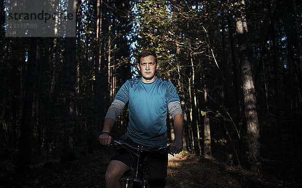 Selbstbewusster Mann sitzt auf Mountainbike gegen Bäume im Wald