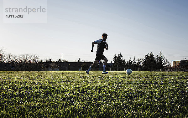 Mann übt Fußball auf Grasfeld gegen klaren Himmel im Park bei Sonnenuntergang