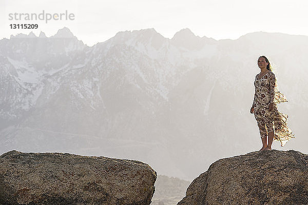 Junge Frau steht bei nebligem Wetter auf Fels gegen Berge