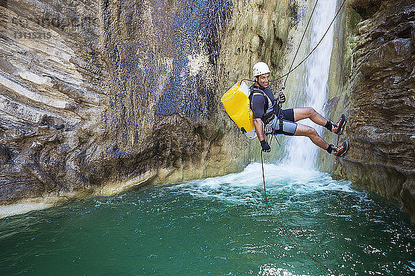 Porträt eines glücklichen Mannes  der am Wasserfall auf einen Berg klettert