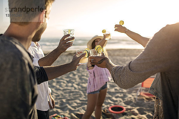 Fröhliche Freunde stoßen am Strand auf Getränke an