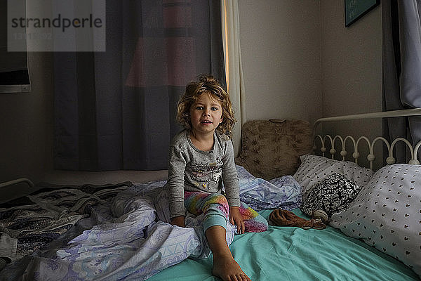 Porträt eines niedlichen Mädchens  das zu Hause auf dem Bett sitzt