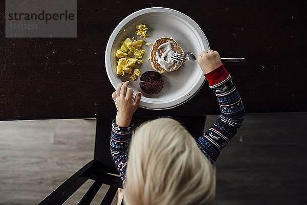 Schrägaufnahme eines kleinen Jungen  der zu Hause am Esstisch sitzt