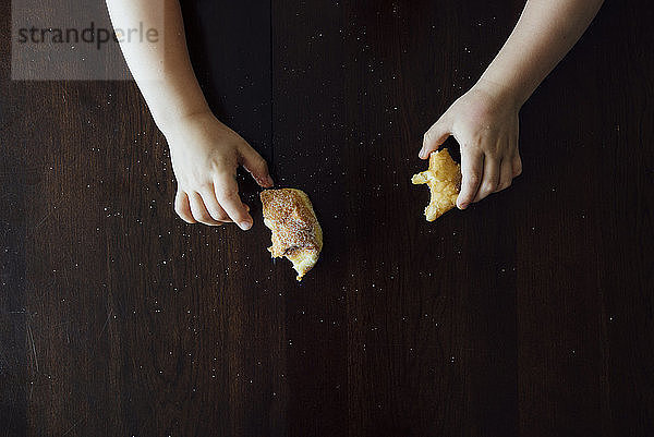 Geschnittene Hände eines Jungen  der zu Hause Brot auf dem Tisch hält