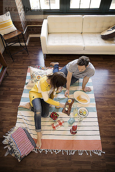 Schrägaufnahme eines Paares  das zu Hause auf einem Teppich sitzt und Essen isst