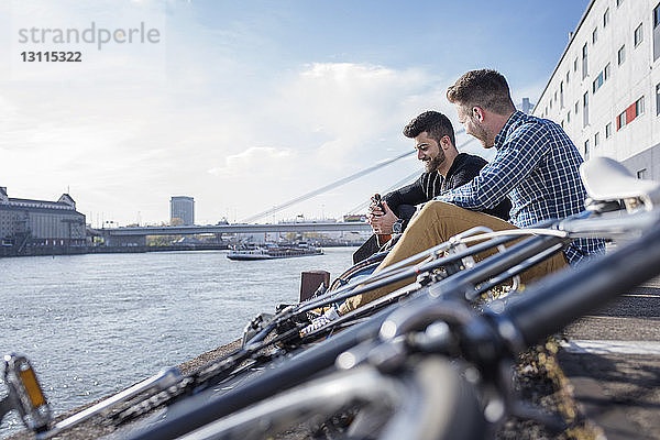 Freunde sitzen mit dem Fahrrad vor dem Kanal vor klarem Himmel