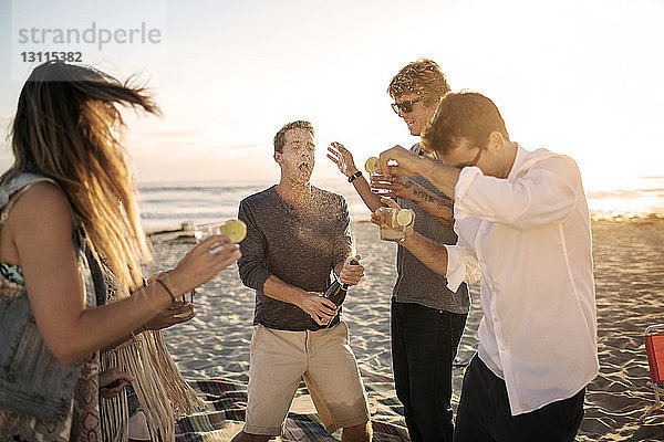 Glücklicher Mann öffnet Weinflasche beim Genießen mit Freunden am Strand