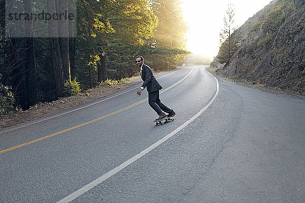 Geschäftsmann beim Skateboarden auf der Straße an einem sonnigen Tag