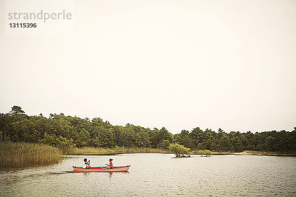 Freunde rudern Boot auf dem See gegen den Himmel