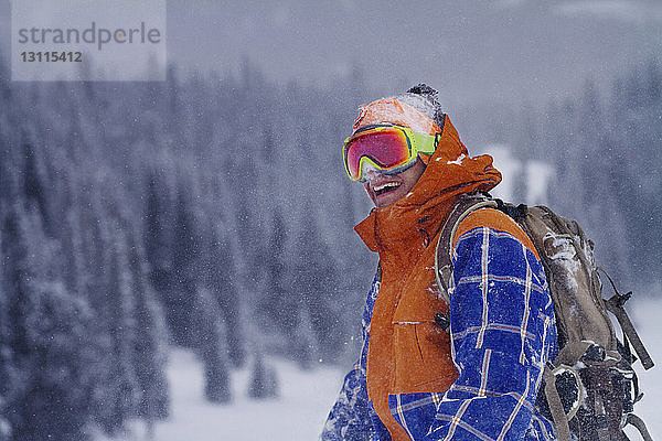 Glücklicher Mann mit Skibrille steht bei Schneefall auf dem Feld