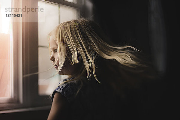 Seitenansicht eines zu Hause am Fenster stehenden Mädchens