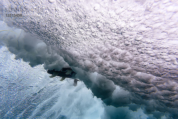 Tiefblick auf ein Surfbrett inmitten der Wellen  die auf den Malediven unter Wasser brechen