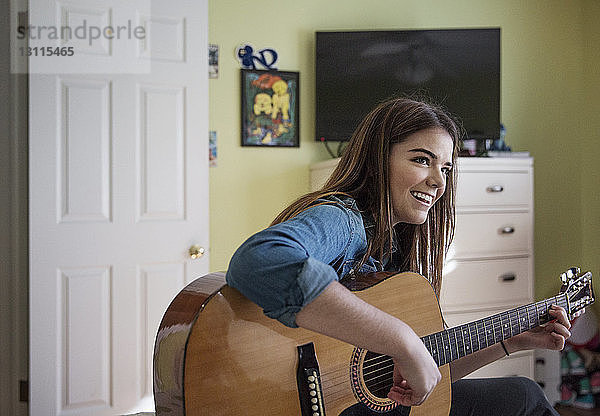 Glückliche Frau spielt Gitarre  während sie zu Hause sitzt