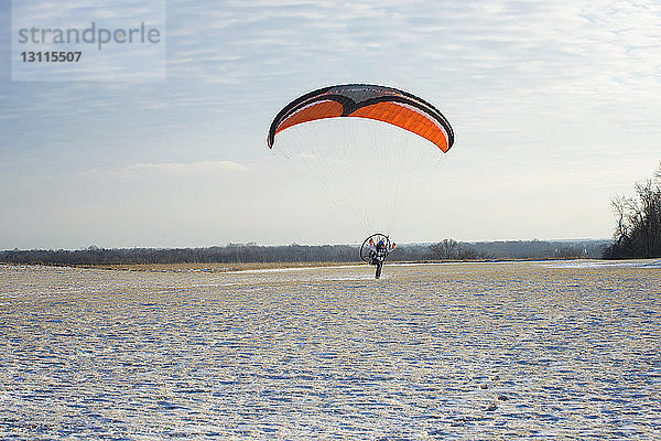 Junger Mann beim Motorgleitschirmfliegen über Feld gegen Himmel