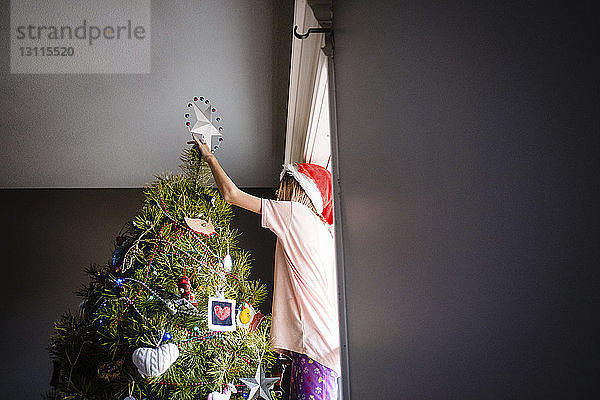 Niedrigwinkelansicht eines Mädchens  das zu Hause den Weihnachtsbaum schmückt