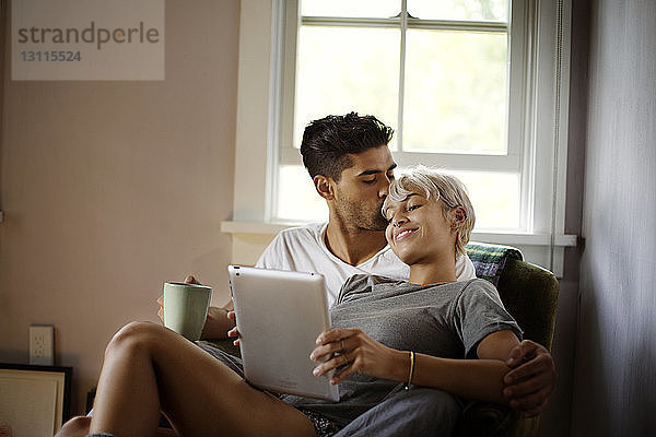 Mann küsst Frau mit Tablet-Computer zu Hause