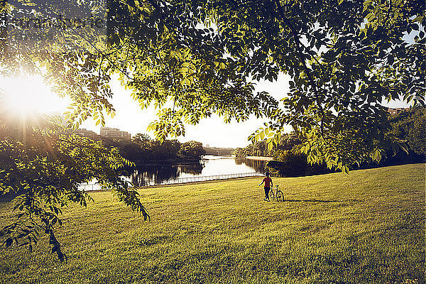 Mann mit Fahrrad auf Grasfeld am See im Park bei sonnigem Wetter