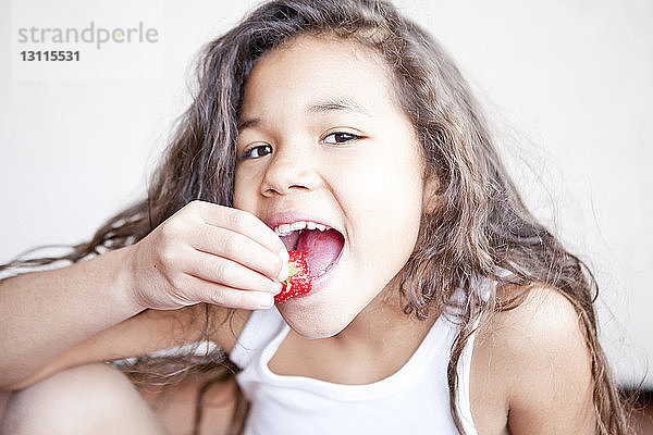 Porträt eines glücklichen Mädchens  das zu Hause Erdbeeren isst