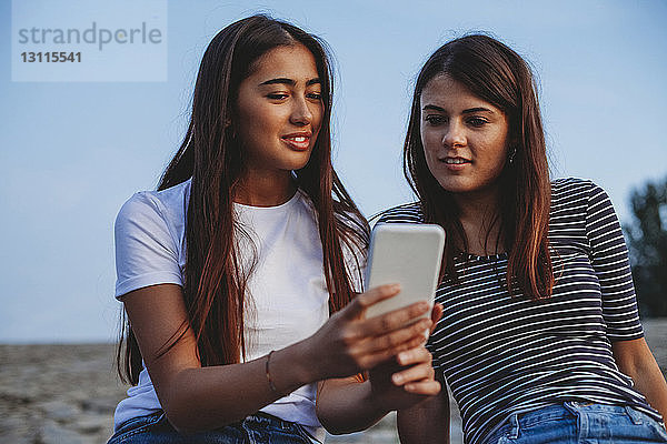 Freundinnen schauen auf Smartphone gegen den Himmel in der Stadt