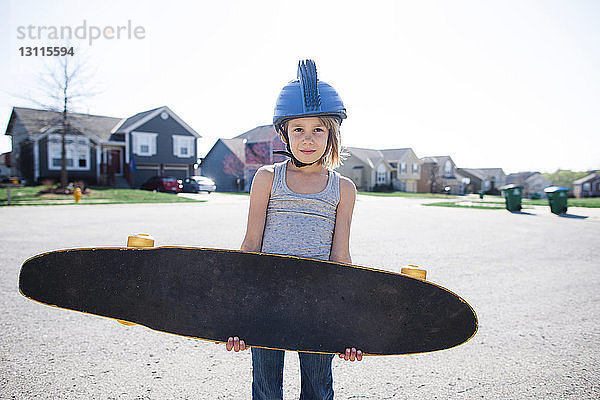 Porträt eines Mädchens mit Helm  das ein Skateboard trägt  während es im Sommer auf der Strasse steht
