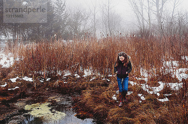 Mädchen geht im Winter auf Grasfeld am See im Wald