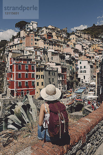 Rückansicht einer Touristin mit Rucksack und Hut beim Blick auf das Stadtbild bei Sonnenschein