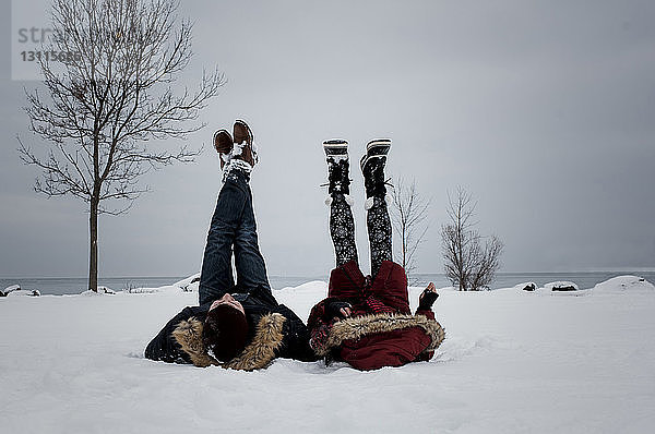 Freunde liegen im Winter am schneebedeckten Strand gegen den Himmel