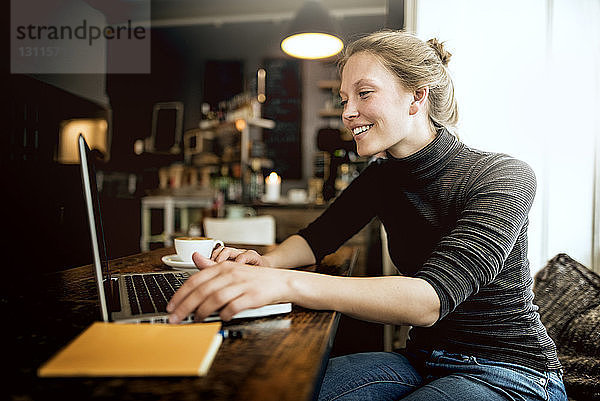 Glückliche junge Frau benutzt Laptop im Café