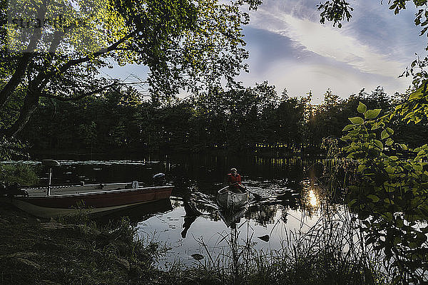 Junge Ruderboot auf See gegen Bäume im Wald bei Sonnenuntergang