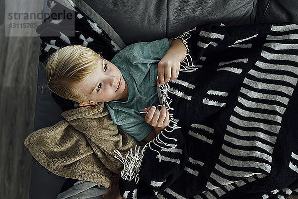 Hochwinkelansicht eines Jungen  der weg schaut  während er zu Hause auf dem Sofa liegt