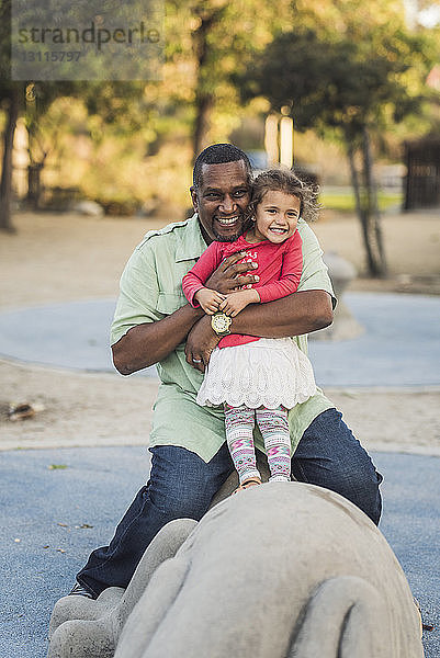 Glücklicher Vater mit Tochter sitzt auf Statue  während er im Park spielt