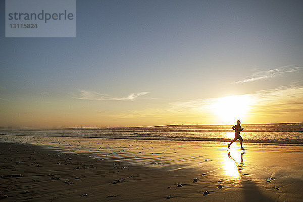 Seitenansicht eines männlichen Athleten  der bei Sonnenuntergang am Strand läuft
