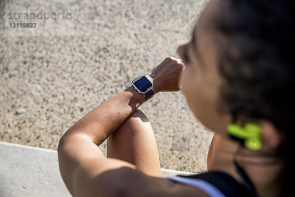 Hochwinkelansicht einer Sportlerin  die eine intelligente Uhr trägt  während sie im Park sitzt
