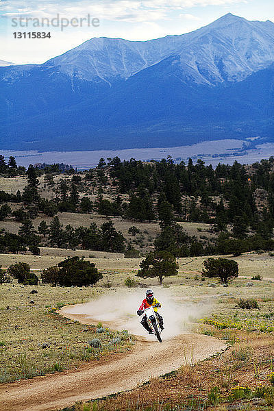 Mann fährt Motorrad auf Feldweg gegen Berg