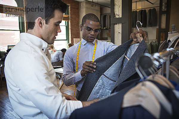 Schneider und Kunden überprüfen Anzüge  während sie in der Werkstatt stehen