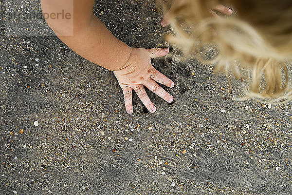 Hochwinkelaufnahme eines Mädchens  das am Strand mit Sand spielt