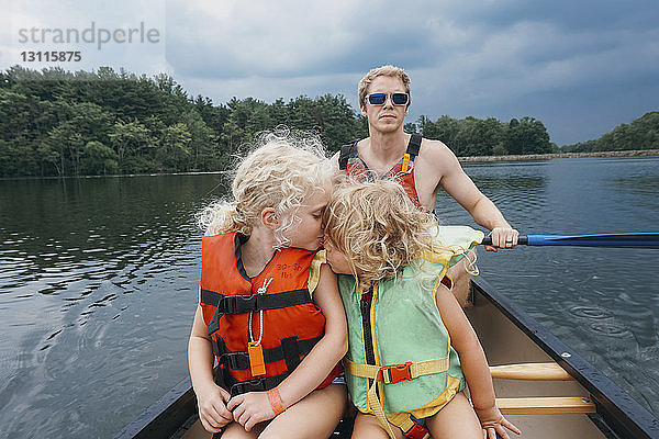 Schwester küsst Mädchen  während der Vater im See gegen Gewitterwolken Kanu fährt