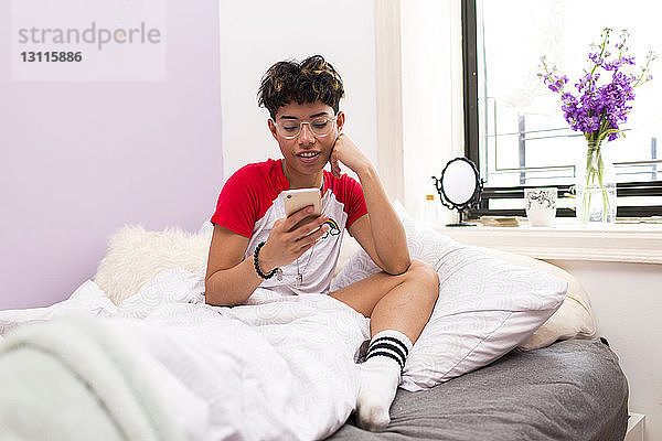 Junge Frau benutzt ein Smartphone  während sie auf dem Bett sitzt