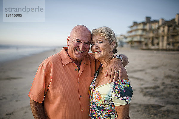 Porträt eines lächelnden älteren Paares  das am Strand gegen den Himmel steht